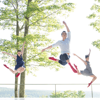 Three dancers are mid-leap on an outdoor stage.