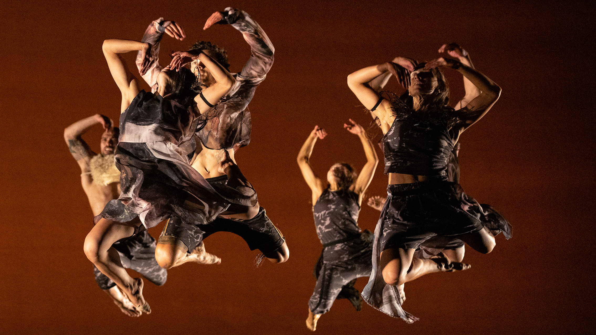 A group of dancers leap in the air against a red backdrop.