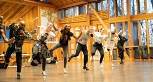 A group of tap dancers rehearse in an indoor studio.