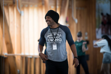 Derick K. Grant wears a beanie and a baseball style tshirt as he grins and looks to his right.