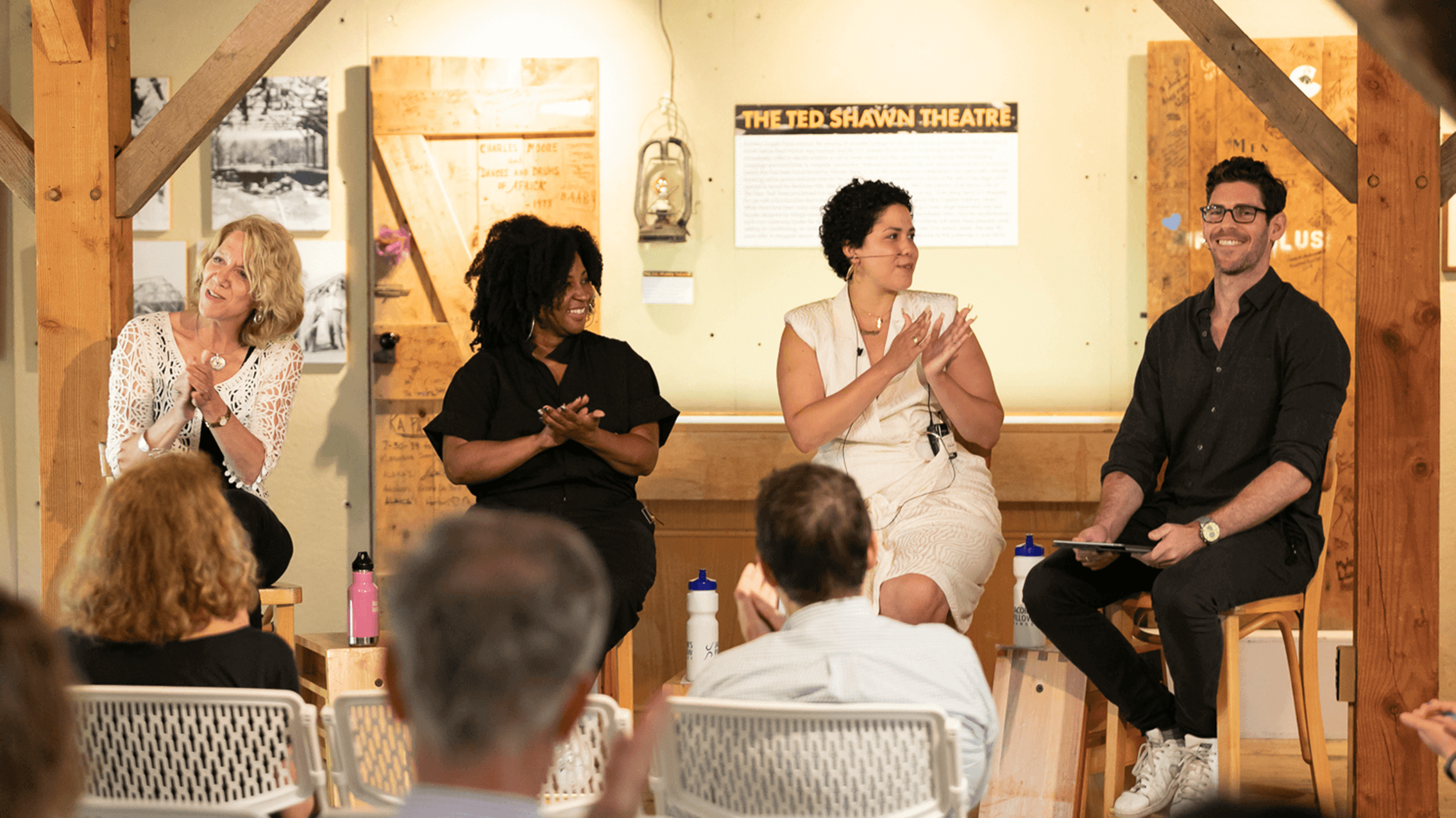 Jacob's Pillow Director Pamela Tatge, Associate Curators Melanie George and Ali Rosa-Salas, and Scholar-in-Residence Brian Schaefer are seated in chairs left to right facing audiences clapping at the end of their PillowTalk, Curatorial Voices.