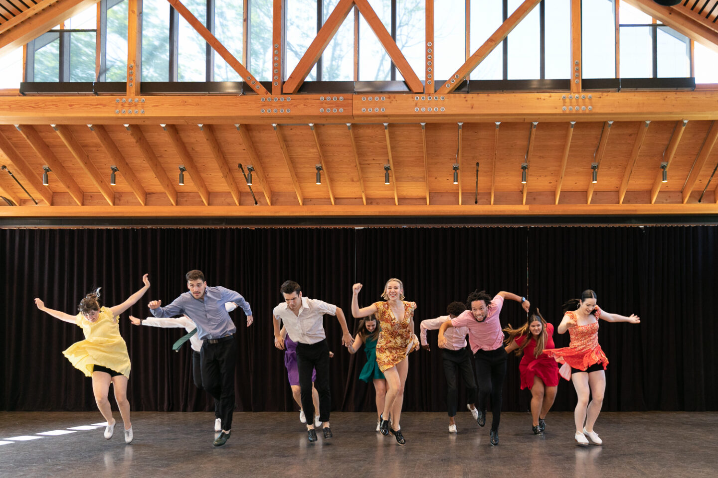 A group of eleven tap dancers perform in a variety of colored outfits facing the camera.