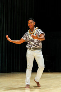 John Mario Sevilla performing Hula dance at 92Y Harkness Dance Center in New York City. He stands and gestures with both hands to his right.