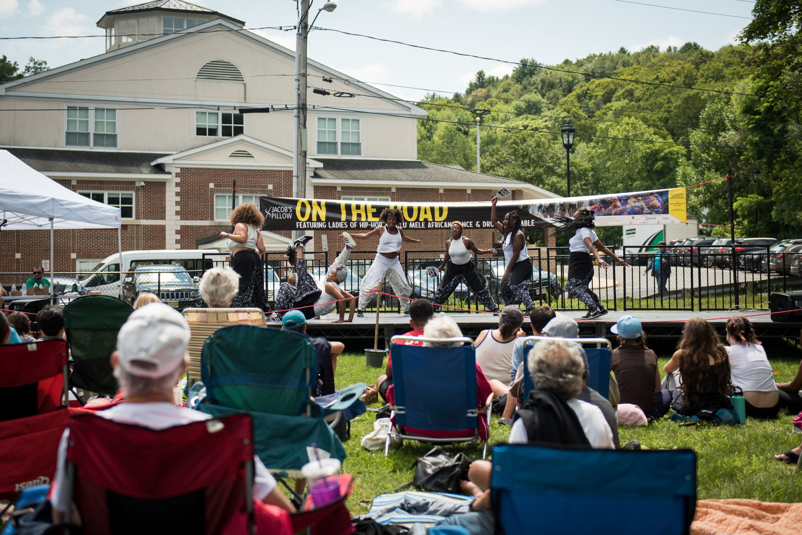 People sitting in lawn chairs face an outdoor stage where a hip-hop group of all women perform.