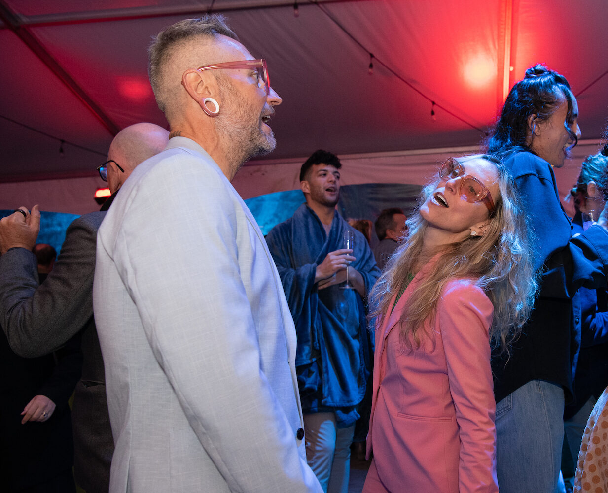 2 people dance at a party, both wearing light pink glasses.