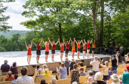 Students in the Contemporary Program Performance hold hands in the air as the audience stands to clap.