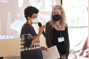 "J.R." Glover and Celeste Miller stand and address the audience. Glover is holding a microphone while Miller looks on.