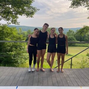 Four dancers wearing all black pose for a photo on an outdoor stage.