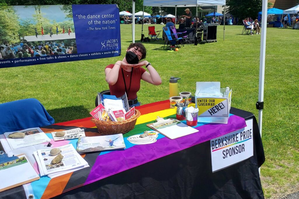 Marketing Staff member Megan Ruffalo sits at a table with a pride flag and flyers.
