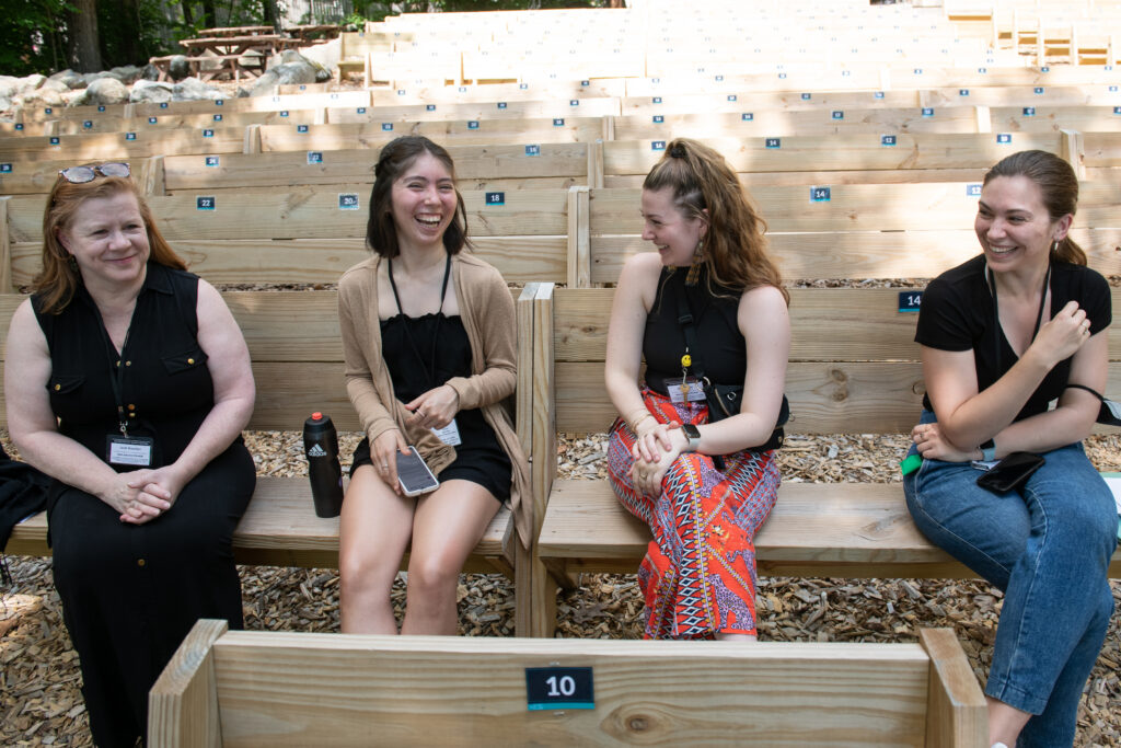 Leah Brandon, Itzel Limon, Sophie Blue, and Bailey McFaden laugh on benches at the outdoor Henry J. Leir Stage.