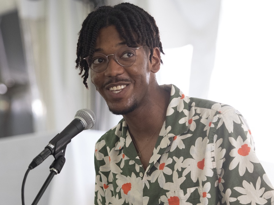 Sterling Harris accepts The Lorna Strassler Award for Student Excellence at Jacob's Pillow. He smiles and speaks into a microphone while holding a check and certificate.