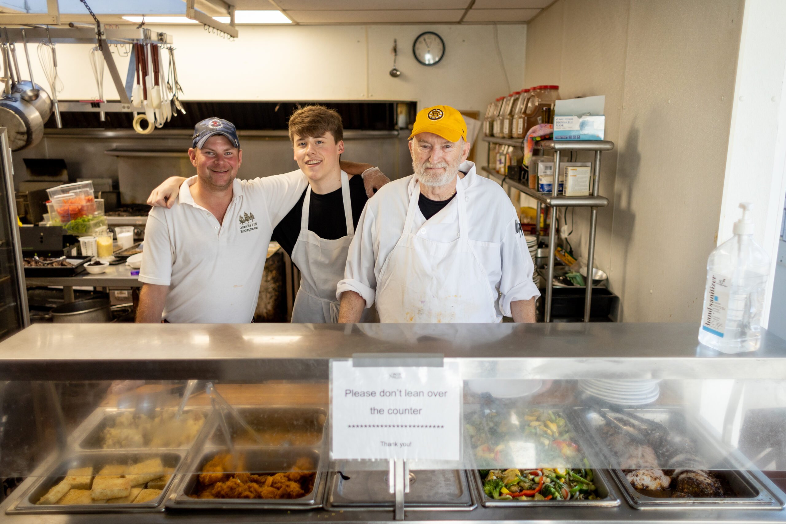 3 men in chef attire smile behind a counter in the Stone Dining Room