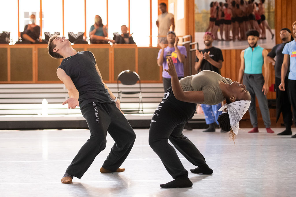 Two dancers face each other and lean backwards, arms bent and held open at their sides.