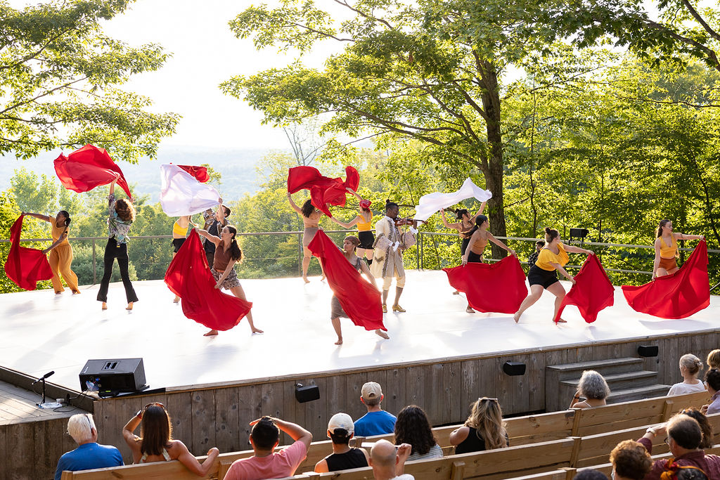 A group of dancers on an outdoor stage wave red and white cloths.