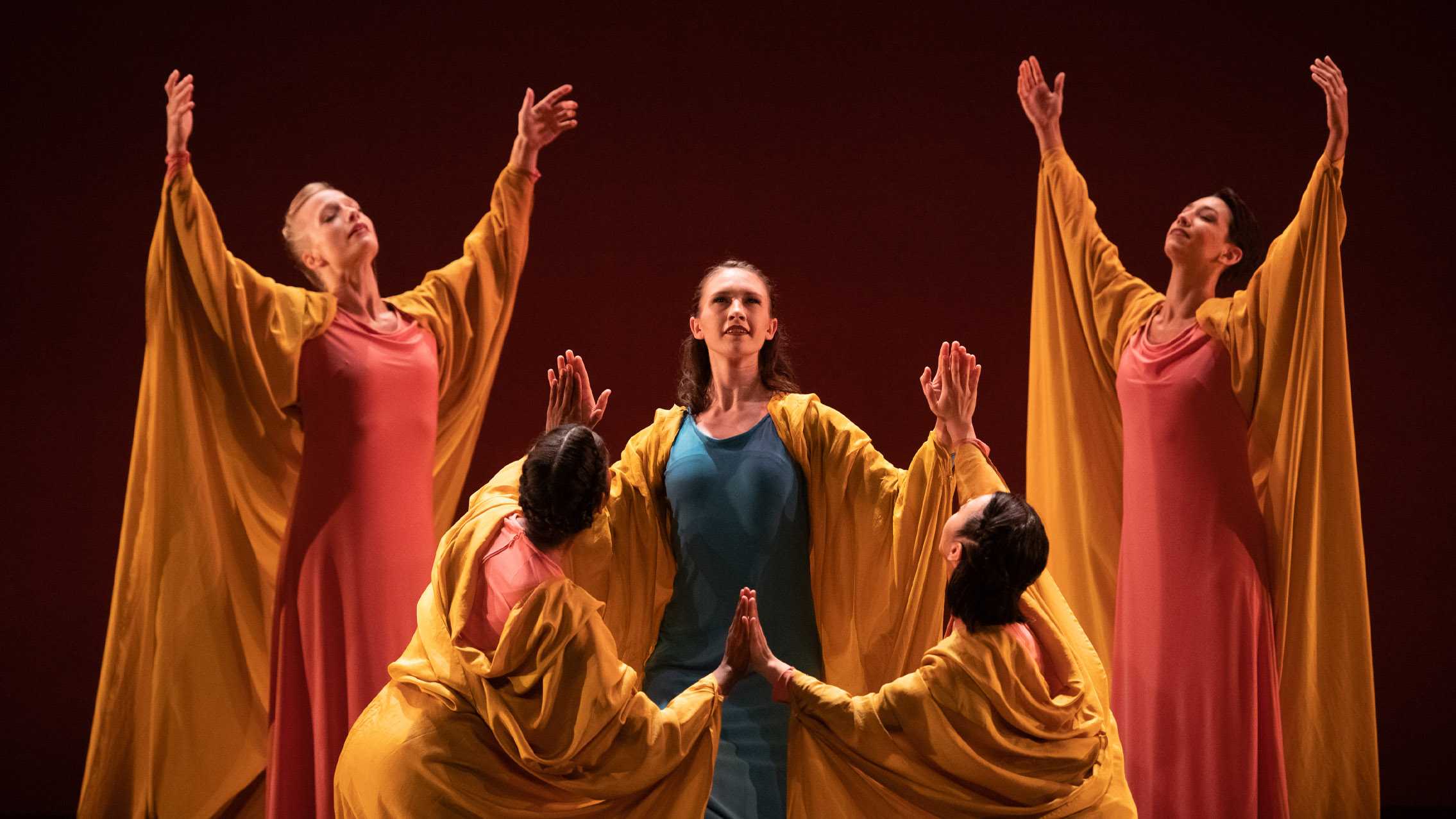 Three femme dancers touch palms while two other hold their arms up behind them.