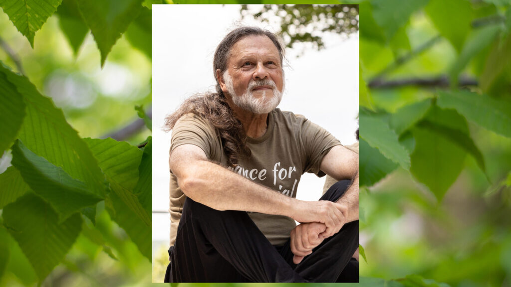 Paul Lewis sitting on Henry J. Leir Stage wearing a green Dance for Social Justice shirt and black pants.