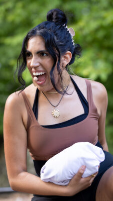 A dancer crouches and sings into her head microphone. She is carrying a bundled white cloth.