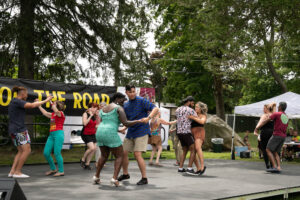 Couples dance on an outdoor stage with their arms around one another.