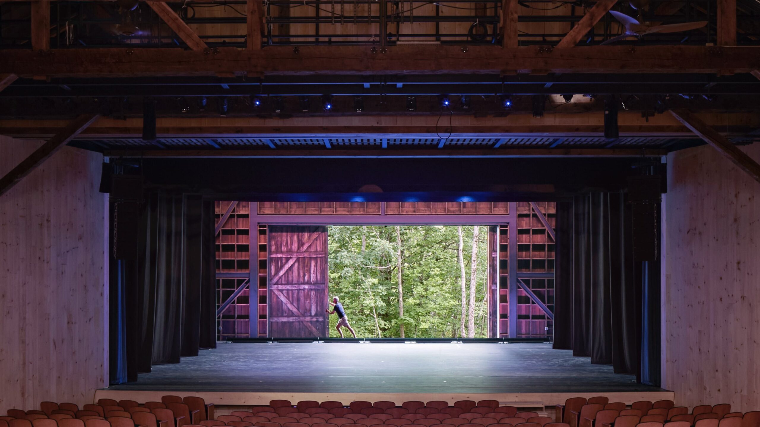 A person pushes open the barn door of the Ted Shawn Theatre, revealing the forest behind the theatre.