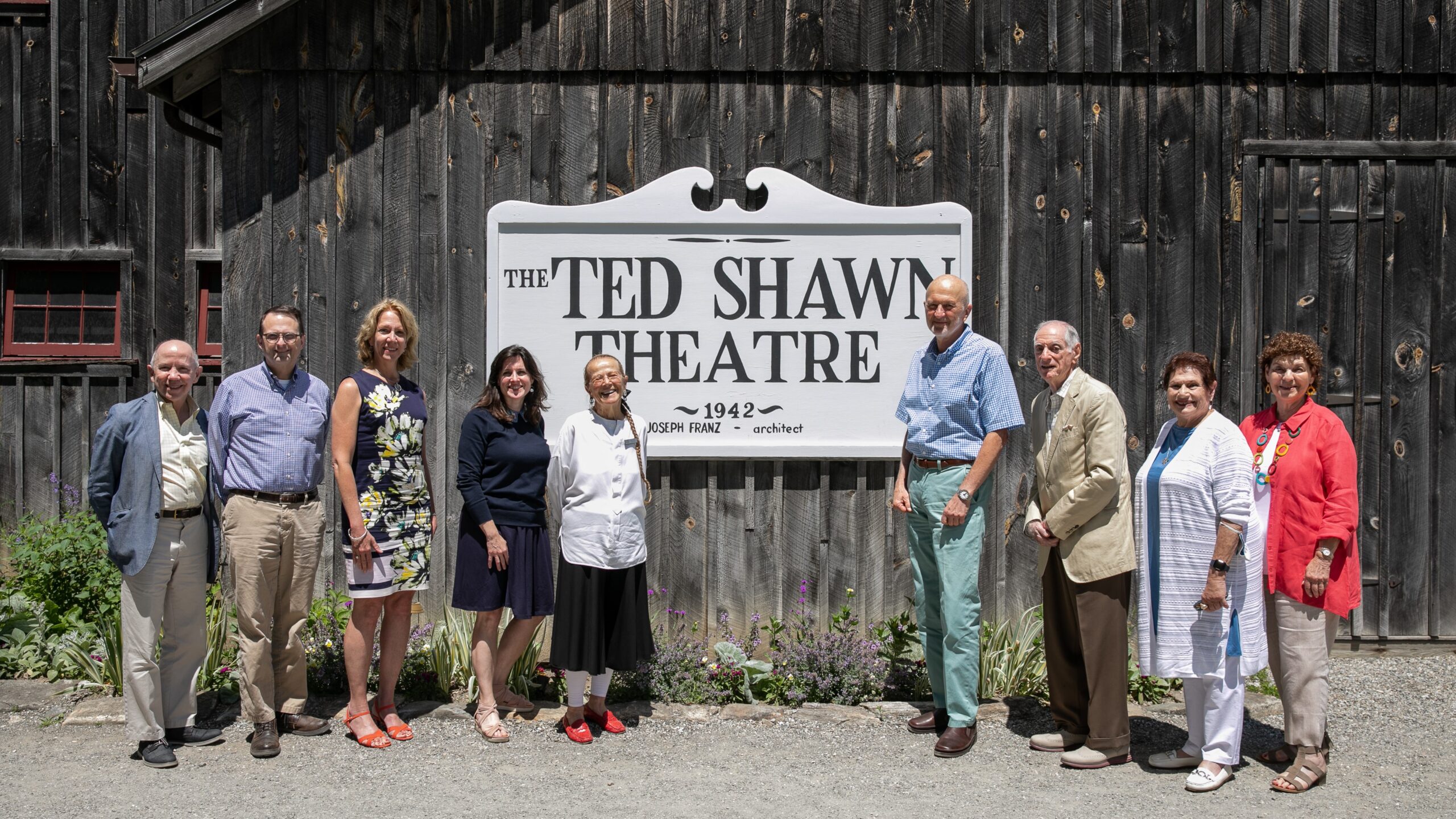 A group of Members and Jacob's Pillow staff stand on either side of the Ted Shawn Theatre sign.