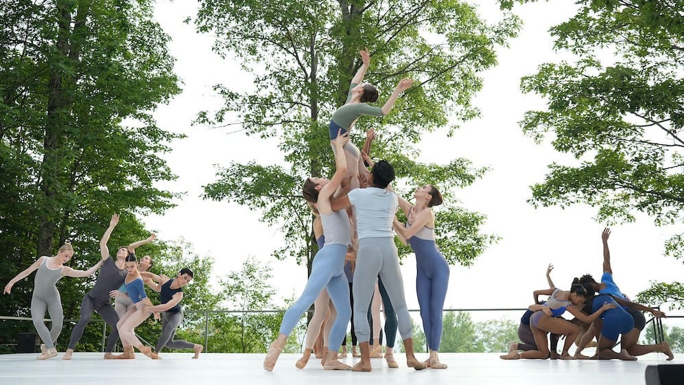 The dancers create three scenes onstage. They all crowd around the center of their circles. The center group holds a dancer up.
