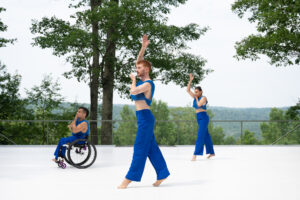 Three dancers from Axis Dance wear blue and face the right. They all have their right arms up.