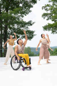 Dancers from Axis Dance face the left and have their left arms above them. They all look upward and wear yellow and beige.