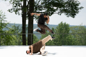 Photo of two dancers from Versa Style. One is doing a tilt on the ground, the other is jumping above him.