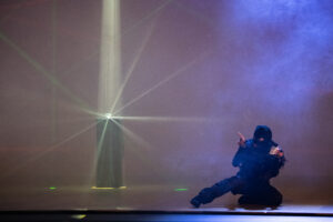 a woman in all black clothing and a mask crouches in from of a diamond