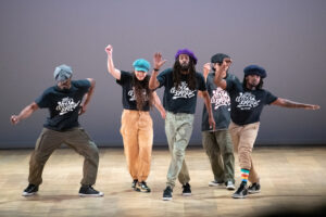 Members of The Hood Lockers stand and dance while facing the audience.