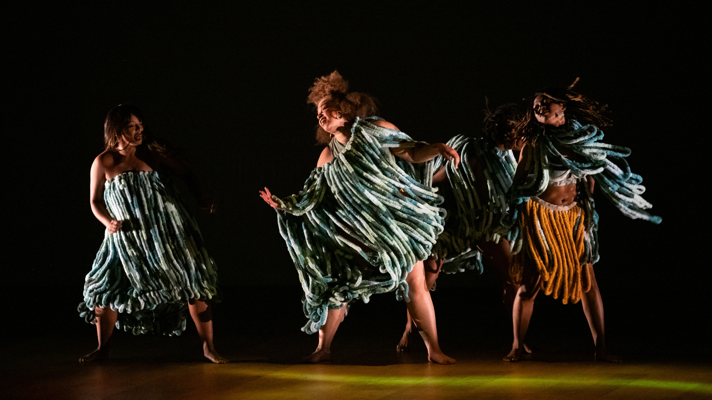 Four Black women in vibrant costumes dance on a warmly lit stage.