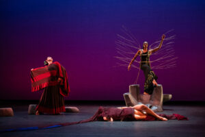 Four dancers pose on a stage with a purple and pink background.