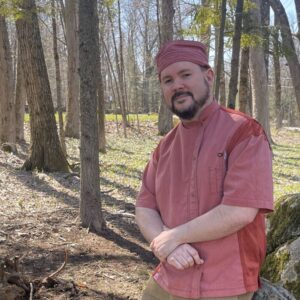 Chef Stephen Will, a white adult man wearing a pink chef's uniform, smiles while outdoors.