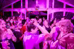 Dance floor of people dancing with others under bright pink lighting.