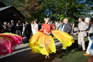Image of a dancers pre-performance costume meant to look like a flower. The dress like costume has flowey gradient yellow and orange petals. The dancer is among other attendees of the gala.